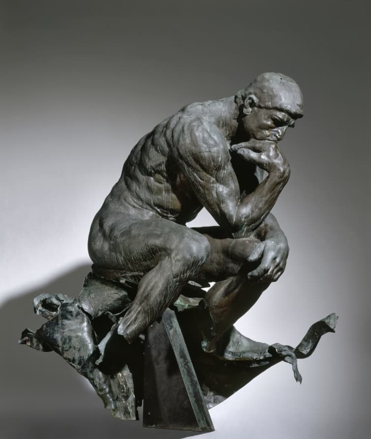 A bronze statue of a man seated, leaning forward with his elbow resting on his knee. 