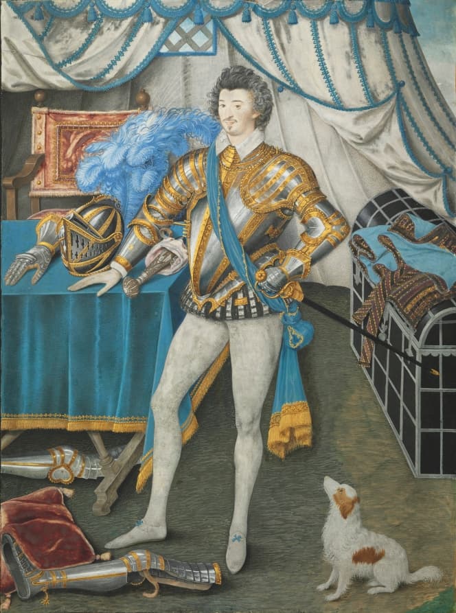 A man in white tights and an ornate silver and gold armor top. A small white and brown dog stares up at him, and his hand rests on a table with additional pieces of armor, including a helmet. Other pieces are strewn on the floor.