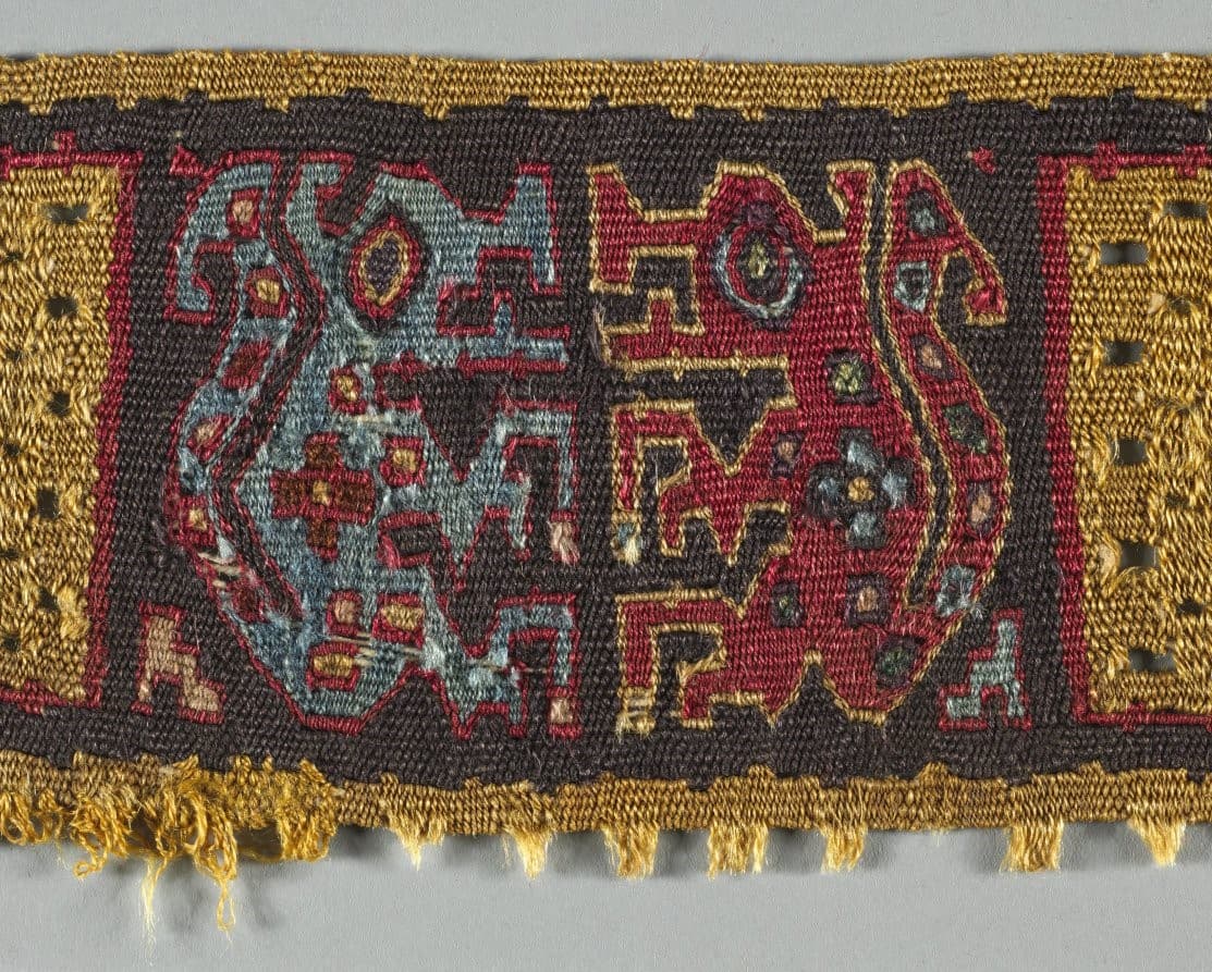 Detail of a woven textile depicting two animal figures, one blue, one red, facing one another.